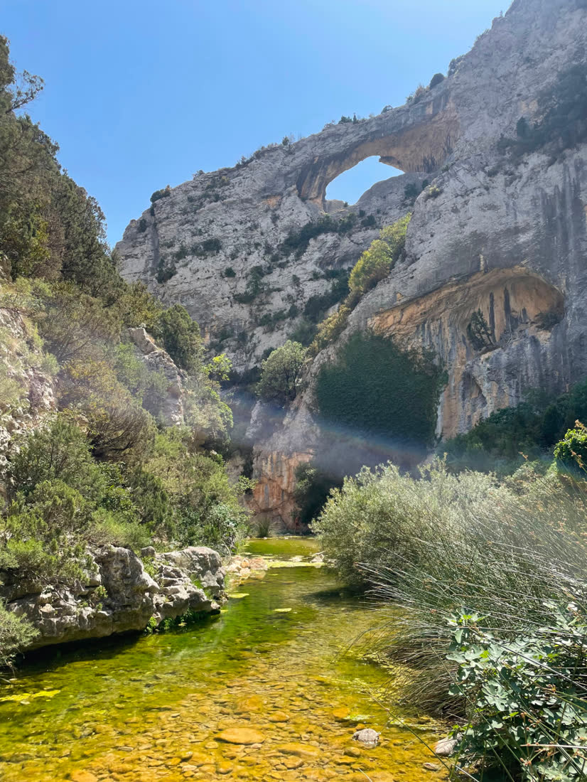 Natural rock arch above a clear stream in Rodellar